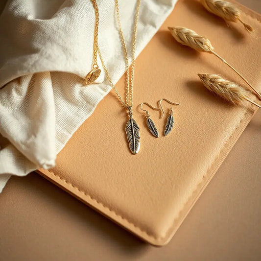 Feather motif necklace, earrings, and bracelet arranged on suede with linen and soft golden light