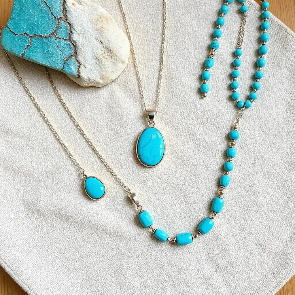 Turquoise pendant and beaded necklaces arranged on neutral fabric with silver accents under soft natural light