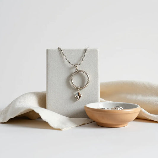 Modern silver necklace, hoop earrings, rings, and a geometric pendant arranged on a minimalist jewelry stand.