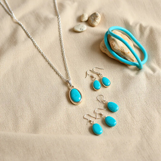 Silver Navajo-style jewelry set with turquoise pendant necklace, drop earrings, and cuff bracelet on neutral fabric