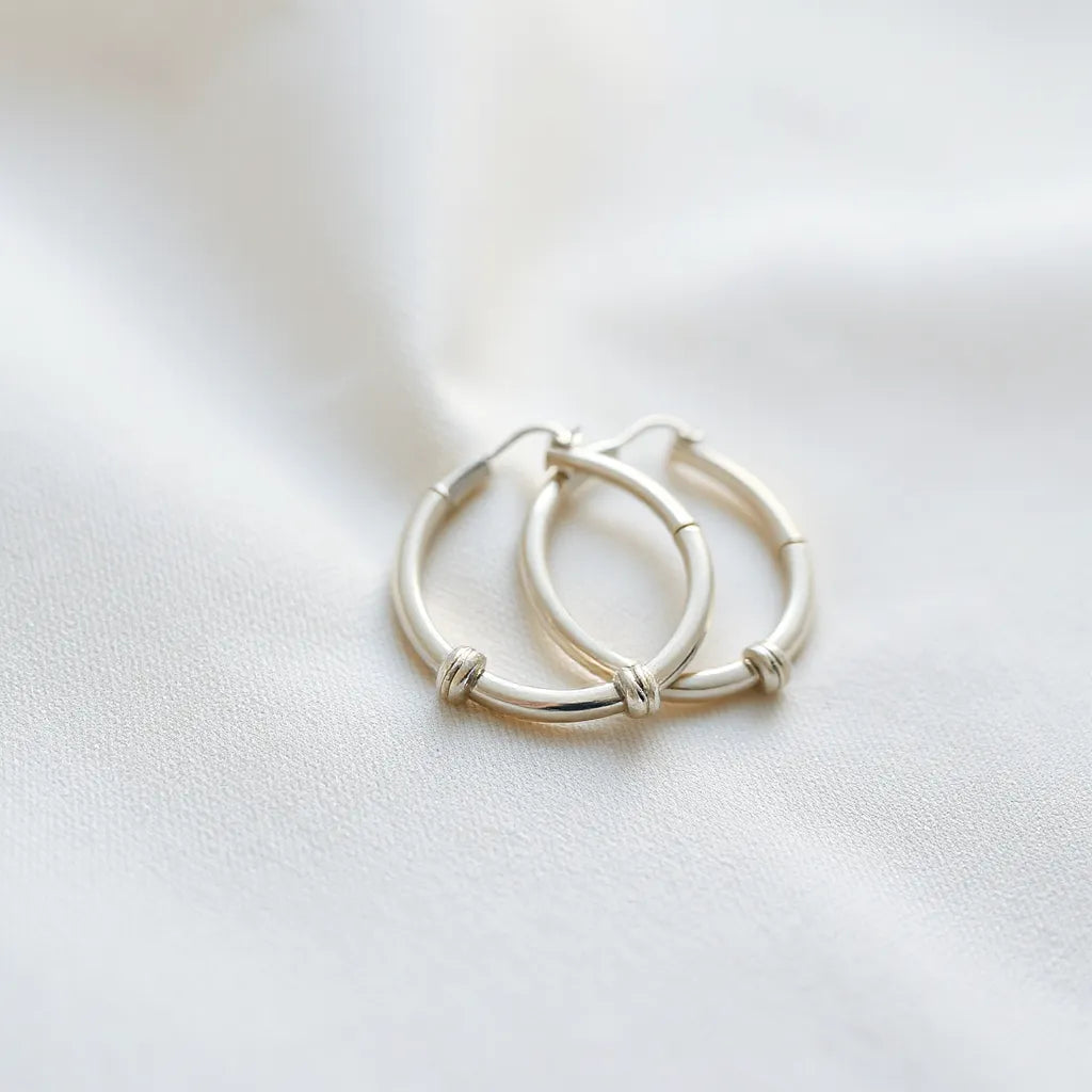 Lightweight silver hoop earrings on a neutral fabric background in soft natural light