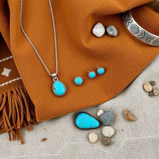 Turquoise pendant necklace with matching earrings and cuff on tan woven fabric with desert stones