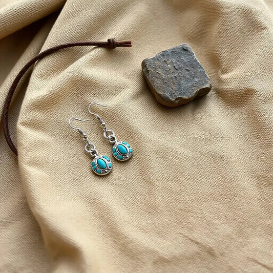 Silver-toned western inspired earrings with concho and turquoise-inspired accents on warm neutral fabric